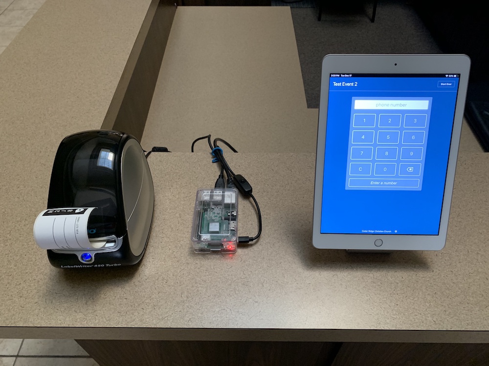 Dymo printer next to a Raspberry Pi computer and an iPad running Planning Center Check-Ins